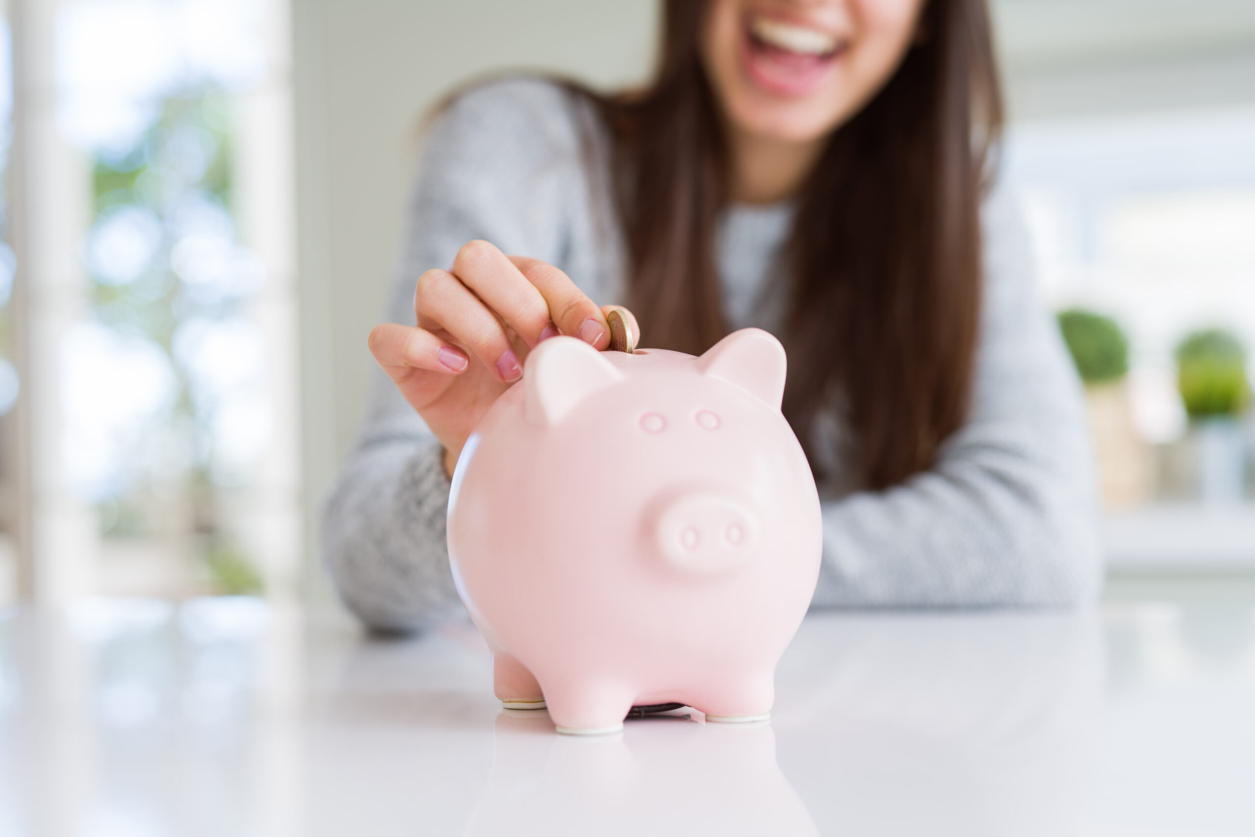Woman dropping coin into a piggy bank container.