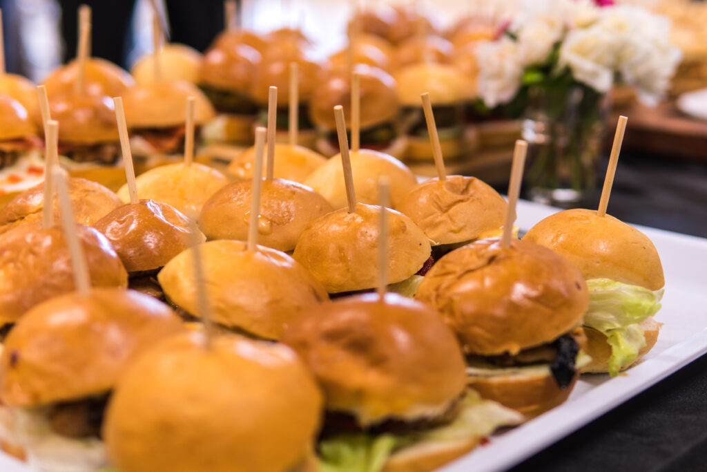 tray of small burgers on a table with black table cloth, National Hamburger Day.